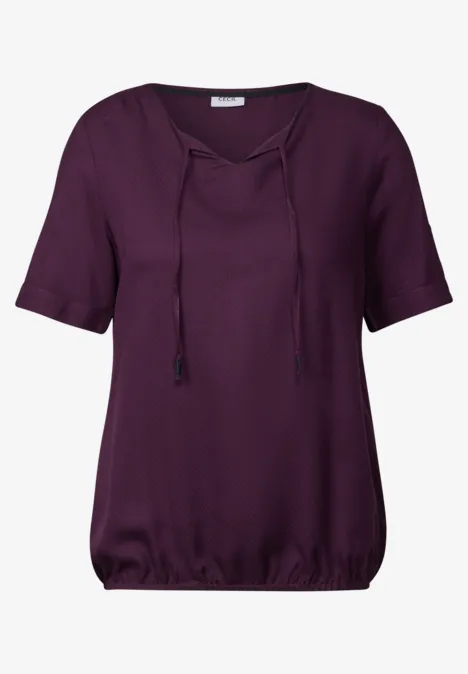 Lila Bluse mit kurzen Ärmeln und Bindebändern am Ausschnitt.